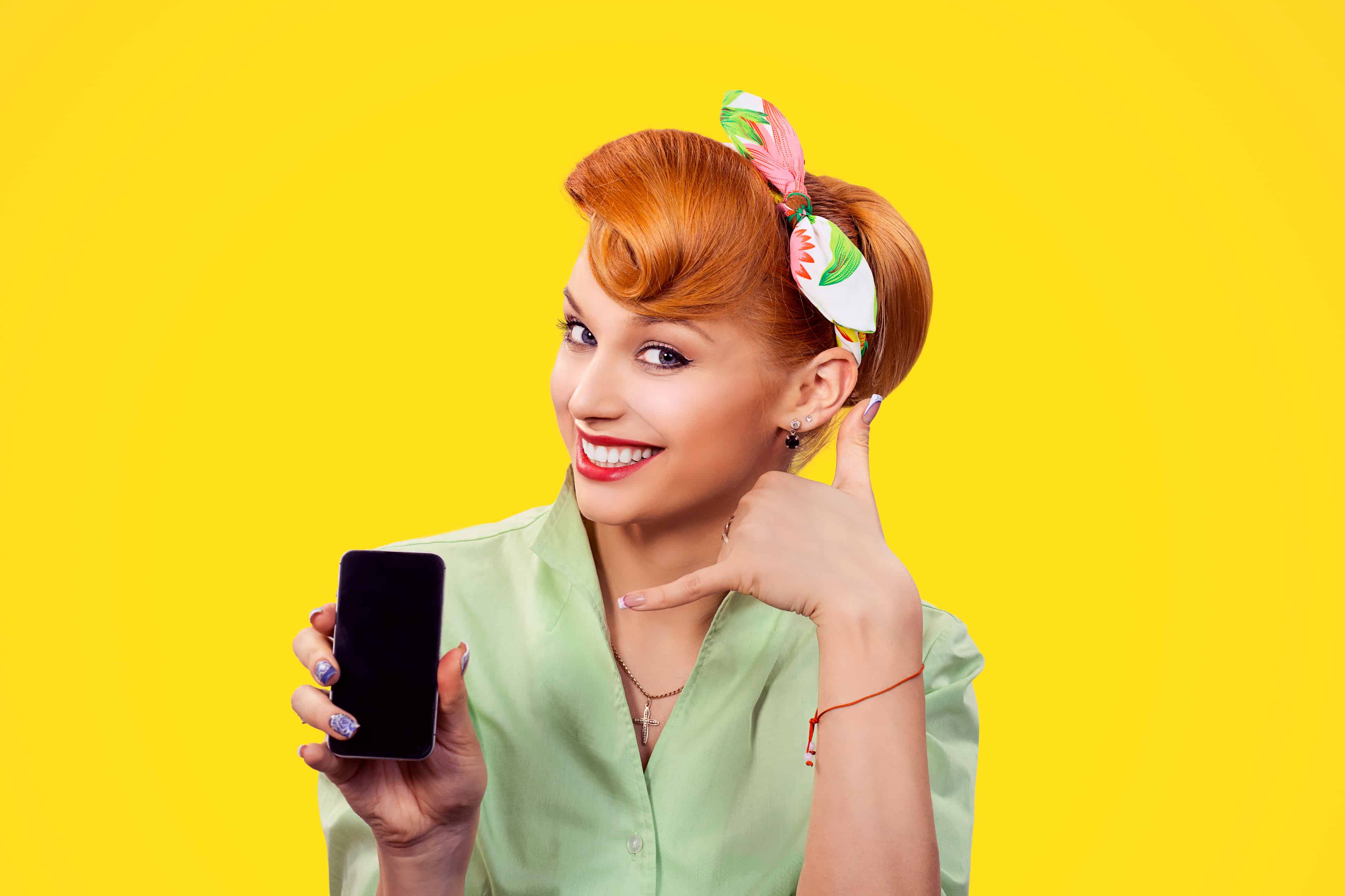 Woman with red hair and green shirt holding a phone in a yellow background