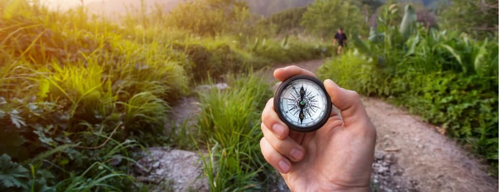 Hand holding a compass with a trail as a background, showing the importance of taking time to work on health & wellness, part of Lisa Cypers Kamen services.