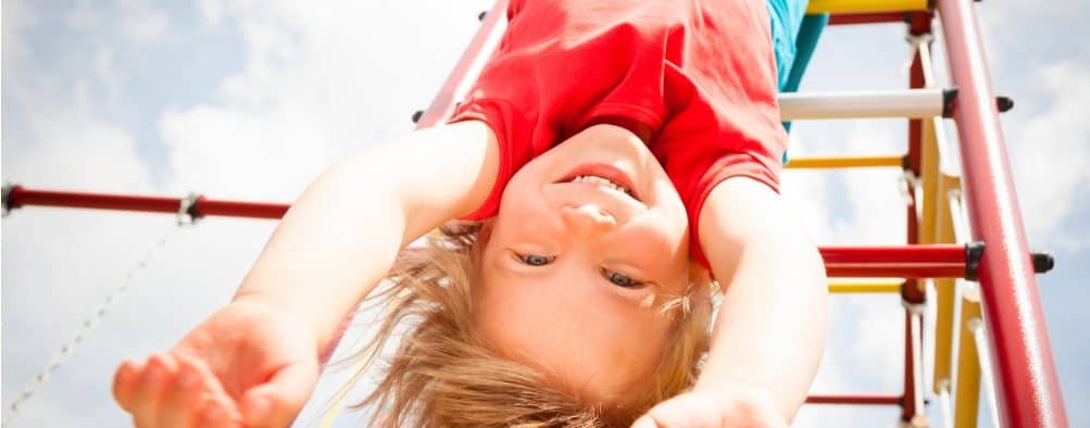 Child with red shirt and blue pants playing on a playground during a sunny day, image of the page of public speaker and life coach expert Lisa Cypers Kamen who develops programs of wellness.