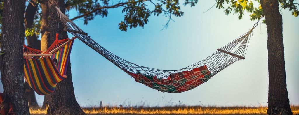 A hammock hanging between two trees with the blue sky as a background, image of one of the programs created by public speaker Lisa Cypers Kamen who works with sustainable well-being and wellness