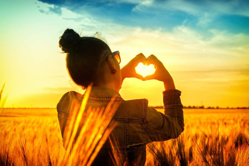 sunset countryside girl adult shows a heart with your hands, referring to happiness what is joy and wellbeing